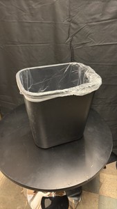 Black Plastic Garbage Can About One and a Half Feet in Height, Comes With Roll of Garbage Bags