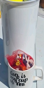 lot of new and used golf balls with tees and coffee cup