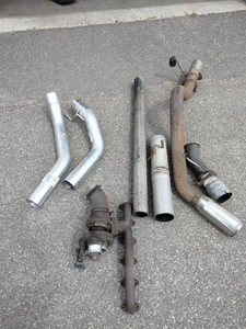 Exhaust manifold with a turbocharger attached, along with various 4 straight and bent pipes, a muffler or resonator, and a tailpipe tip.