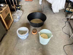 Plastic, ceramic, and metal planters including large black plastic tub and decorative blue and white ceramic pot with additional containers