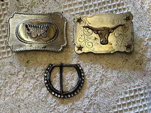 Western-themed belt buckles including intricate wagon design, longhorn motif, and a rhinestone-studded buckle