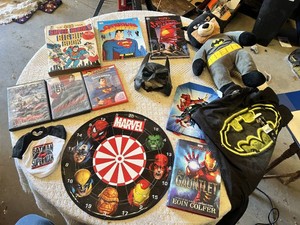 Superhero Collection including DVDs, Books, and Toys DVDs like Avengers Age of Ultron and Superman Red Son, books such as Iron Man The Gauntlet by Eoin Colfer, a Batman plush toy, a Marvel dartboard