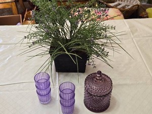 Artificial lavender plant in a black pot, set of purple glasses, and a purple glass container with lid