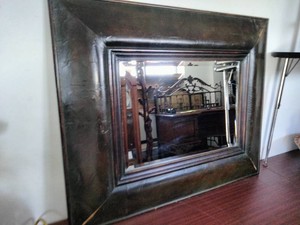 Accent wall mirror features a heavy, dark-finished frame that resembles faux leather