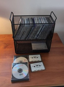 Assorted Music CDs Cassette Tapes in Black Metal Mesh Basket