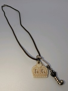 Juicy Couture necklace, brown braided cord with a safety pin charm holding a crown pendant and a rhinestone J charm