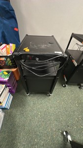Black metal media cart on wheels with cord and doors.