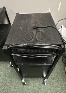 Black metal media cart on wheels with cord and doors.