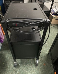 Black metal media cart on wheels with cord and doors.