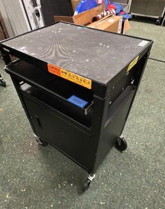 Black metal media cart on wheels with cord, pull out tray and door.