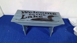 small bench that says welcome to the lake
