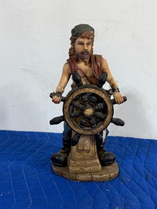 vintage resin pirate captain figurine standing at a ships helm wheel. This detailed collectible depicts a bearded sea captain wearing a vest and head bandana, steering his vessel from a wood-textured base