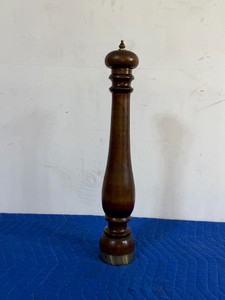 vintage oversized wooden pepper mill featuring a classic baluster-shaped turned silhouette, a metallic grinding base, and a decorative brass finial at the top.