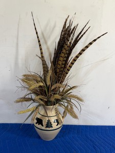 rustic floral arrangement featuring pheasant feathers and wheat stalks housed in a decorative ceramic jug