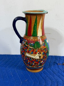 vintage Mexican folk art terracotta pitcher, typically handcrafted in regions like Guerrero or Puebla. It features a hand-painted glossy finish depicting a vibrant village festival procession or storyteller scene