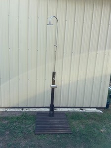 freestanding rain-style outdoor shower with a slatted wood platform.