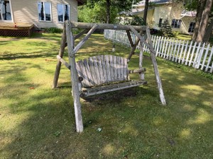rustic wooden swing features curved slats and weathered bark-covered log supports