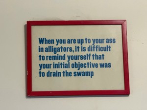 motivational wall art features the proverb When you are up to your ass in alligators, it is difficult to remind yourself that your initial objective was to drain the swamp in a simple red frame.