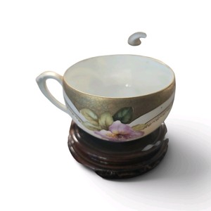 Vintage porcelain teacup features a delicate hand-painted floral design with significant gold gilding along the rim