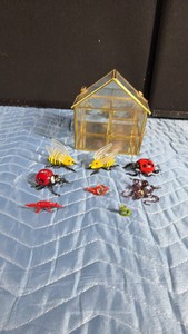 small, house-shaped glass display terrarium or trinket box with a gold metallic frame with glass blown figurines