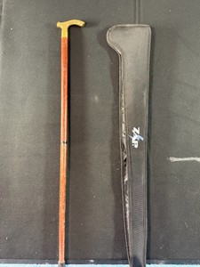 Vintage-style wooden walking cane with a polished brass derby handle alongside its custom black nylon carrying case.