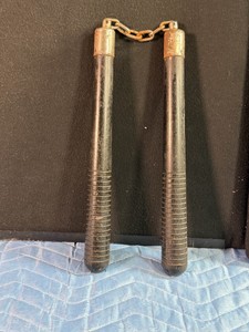 Pair of vintage wooden nunchucks (or nunchaku), a traditional Okinawan martial arts weapon consisting of two sticks connected by a short chain or rope.