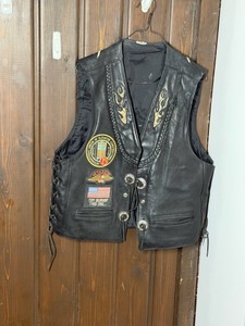 Black leather motorcycle vest features decorative patches and metal pins.