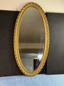 Vintage oval wall mirror featuring an ornate, gilded gold frame with a detailed, beaded pattern