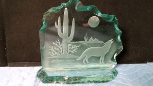 signed green glass sand carved coyote howling at the moon in a desert landscape