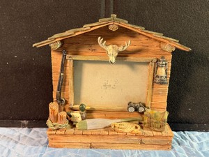Rustic log-cabin-style picture frame features 3D molded outdoor sporting accents like a deer skull mount, rifle, and lantern.