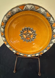This vibrant yellow and silver-accented decorative plate is a handcrafted Moroccan ceramic piece from Safi featuring intricate metalwork detailing including metal display stand