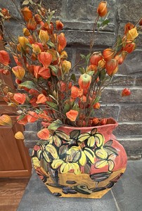 a colorful, hand-painted ceramic art pottery vase featuring vibrant yellow and black floral motifs set against a reddish-pink and yellow base.