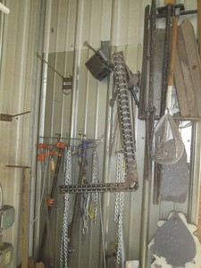 Content hanging on wall to include bar clamps, metal tripods, welding aids, metal plates chains and more
