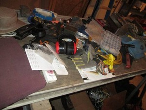 Content on tabletop to include rifle cleaning supplies, drill bits, hardware organizer, misc hand tools, wheelbarrow tires, heavy duty extension cord, road maps, thick rope, office supplies and more