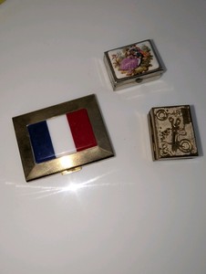 Collection of three vintage small metal containers  gold-tone French tricolor flag case, a floral-art lidded box, and an embossed sewing-motif trinket box