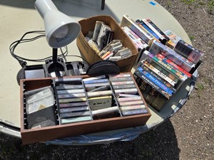 Assorted Vintage Cassette Tapes and VHS Movie Collection including Cassette Rack, Desk Lamp, and Accessories