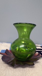 Green glass vase, on top of a ceramic leaf.