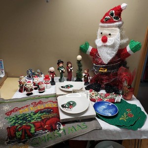 Christmas decoration collection featuring Santa figurines and candles, ceramic plates, a Christmas-themed towel, and wooden caroler figures.