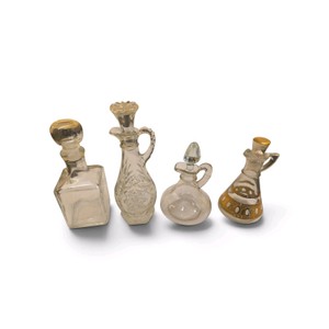 Four distinct vintage and antique glass cruet bottles and decanters featuring various shapes, handles, and decorative stoppers.