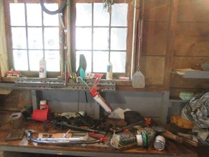 Content on benchtop including hack saw, pry bar, specialty wrench, hedge trimmer, grill brush, cable wire, fishing line, tire iron and more