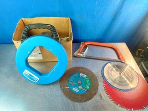 Blue IDEAL Tuff-Grip fish tape reel, an orange hacksaw, a brown abrasive cut-off wheel, and circular saw blades resting on a table