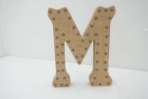 burlap covered wooden letter M accented with brass nail head trim