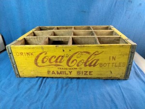 Vintage yellow and red Coca-Cola wooden crate designed to hold 12 family-size bottles from the 1960s.
