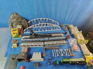 An assortment of model railroad layout pieces, including gray plastic curved chord truss bridges, a model crane, scenery rock molds, track sections, and small buildings.
