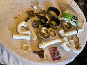 Lot of plumbing supplies including PVC pipes, rubber couplings, and sink strainers