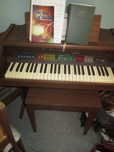 Vintage Genie Lowrey electric organ with wood bench and music shown