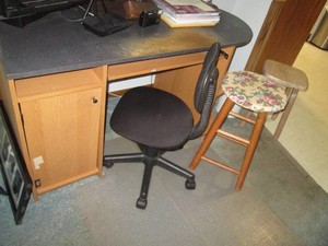 Uniquely shaped desk with rounded end cap style shelving , floor mat, rolling office chair, (2) wood stools and trash bin