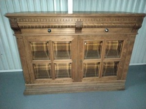 A vintage wooden buffet or display cabinet with two glass-paneled lower doors and upper drawers featuring round knobs