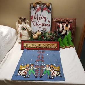 Christmas and holiday-themed decorations including a wooden Merry Christmas sign, Silent Night plaque, angel figure, green wooden trees, and festive table runner