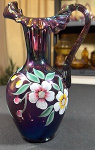 VINTAGE Signed Fenton hand-painted iridescent purple carnival glass pitcher featuring a ruffled crest rim and floral motif.